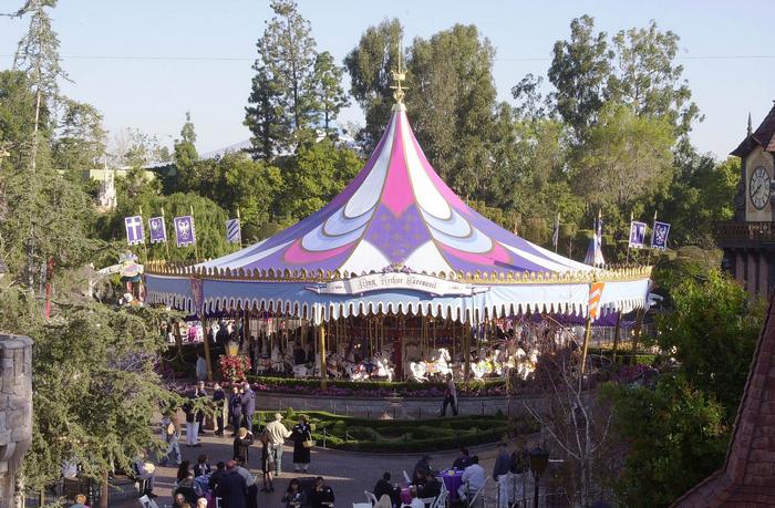 King Arthur Carrousel featuring its vibrant tented roof, nestled among trees and fans in Disneyland’s Fantasyland.