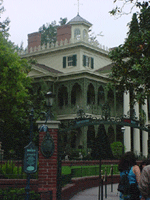The Haunted Mansion with signature iron gates, lush landscaping, and guests entering at New Orleans Square in Disneyland.