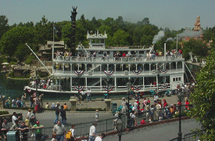 The Mark Twain Riverboat, decked in festive bunting, cruises through Frontierland as Disneyland guests look on under sunny skies.