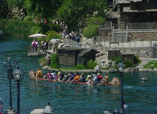 Guests paddle a canoe along the Rivers of America in Disneyland’s Critter Country, passing rustic lodges and lush landscapes.