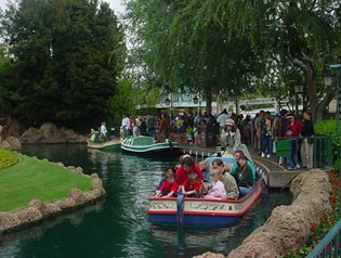 Families enjoy a scenic boat ride along the park's canal, with guests lining up near the dock amidst lush landscaping.