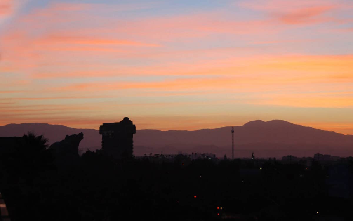 A brilliant sunset over Disney California Adventure, with park landmarks silhouetted and twinkling lights welcoming nighttime magic.