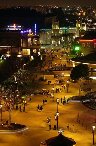 Downtown Disney District plaza glowing at night with guests strolling under vibrant lights and festive street lamps.