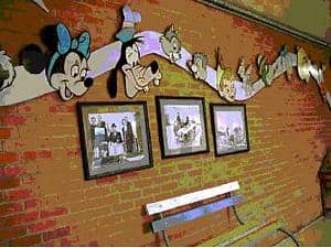 Classic Disney icons and vintage photos brighten a brick wall, creating a nostalgic scene above a themed bench.