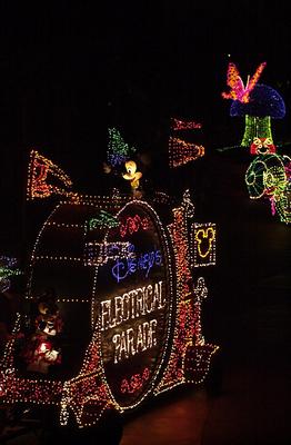 The Electrical Parade float glows with vibrant lights, featuring favorite Disney characters and the famous illuminated parade sign.