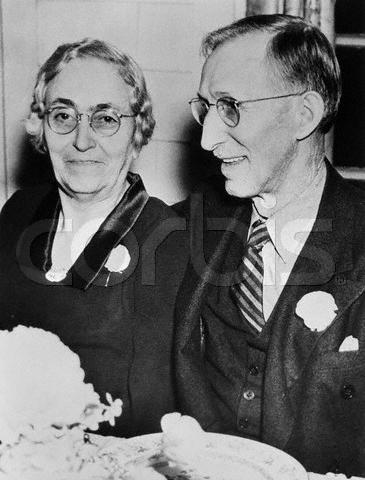 A cheerful senior couple in elegant attire, both in glasses, enjoy a magical moment at a flower-adorned table at Epcot.