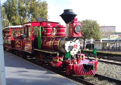 Classic red steam train at Disneyland’s Main Street, parked on the tracks amid trees and vintage buildings—iconic photo op spot.
