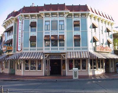 A charming blue and white Victorian storefront with striped awnings sits at the corner of Main Street USA in Disneyland.