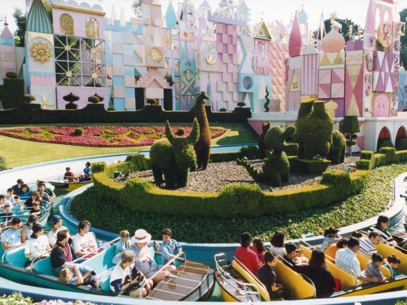 Guests cruise by vibrant animal-shaped topiaries on Storybook Land Canal Boats in Disneyland's pastel-hued Fantasyland.