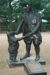 Bronze statue of Lt. Harry Colebourn greeting Winnie the Bear, honoring Winnie the Pooh’s origins; trees and a fence behind.