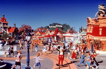 Mickey Mouse welcomes guests at Disney World, surrounded by families in a lively, colorful cartoon-themed park setting.