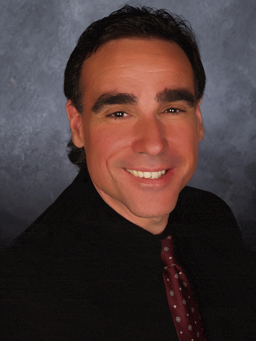 A cheerful park host in a sharp suit and fun tie greets guests against a sleek, theatrical backdrop.