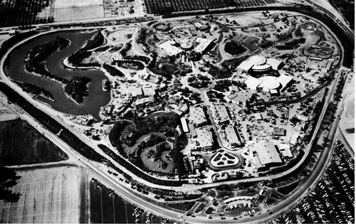 Vintage aerial black-and-white view of Disneyland, bordered by sprawling parking lots and undeveloped fields.