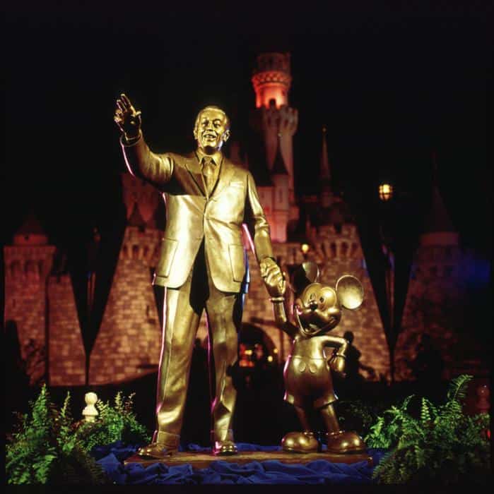 Iconic Partners statue of Walt Disney and Mickey Mouse holding hands at Disneyland, with the castle glowing beautifully at night.