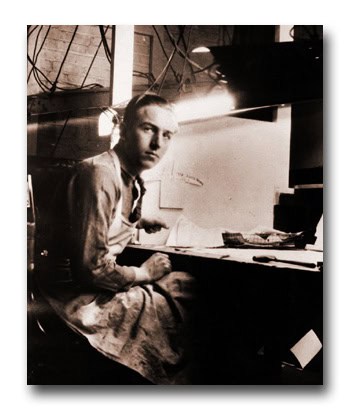 An Imagineer in an apron sits at a workshop table, glancing at the camera amid the softly lit magic of a Disney creative space.