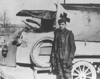 A costumed actor as a young medic poses beside a vintage Red Cross ambulance, recreating early 1900s scenes at the park.