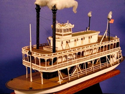 Replica of a classic white river steamboat with smokestacks and an American flag, like the iconic Mark Twain at Disneyland.