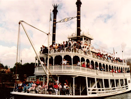 Mark Twain Riverboat carrying guests along the Rivers of America, passing near the Walt Disney Family Museum under a cloudy sky.