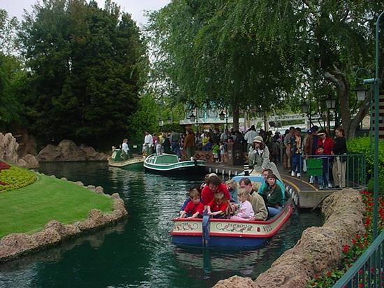 Storybook Land Canal Boats glide past lush greenery as Disneyland fans eagerly await their magical cruise on this classic attraction.