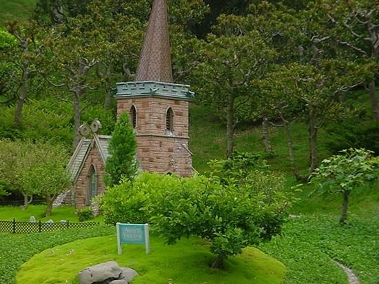 Whimsical stone church with a tall steeple, nestled in lush gardens—just like the charming miniatures at Disneyland’s Storybook Land.