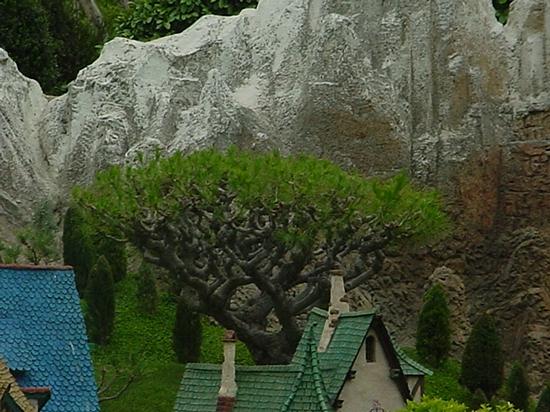 A whimsical tree rises behind Storybook Land rooftops with blue and green shingles, set against Fantasyland’s rocky cliffs.