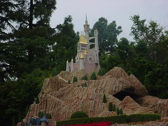 Whimsical Disney castle with golden spires atop a rocky hill, nestled in lush greenery along the Storybook Land Canal Boats.