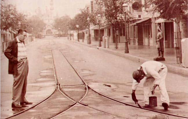 A cast member paints Main Street trolley tracks at Disneyland, evoking the nostalgic charm of vintage Walt Disney era photos.