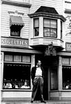 Mickey Mouse, dressed in a sharp suit, poses confidently on Main Street, with charming shopfronts reminiscent of Disney magic.