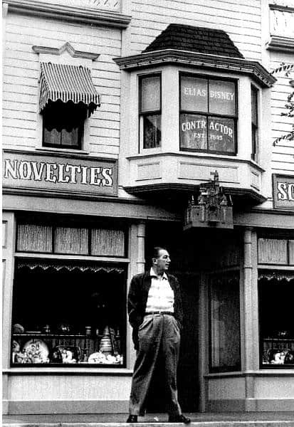 A guest strolls down a Main Street-style sidewalk by charming shop windows topped with a bay window, evoking Disney park magic.