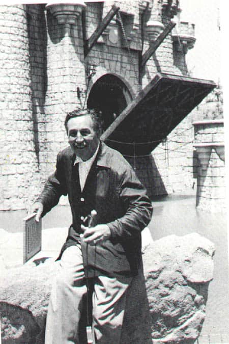 A guest beams while holding a plaque outside a castle with its drawbridge raised, evoking vintage Disney Parks moments.