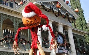 Jack Skellington in a Santa hat poses before his festive Haunted Mansion façade, blending Halloween Town and Christmas magic.