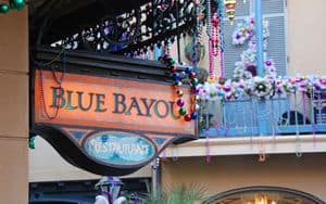 Blue Bayou Restaurant sign decked out in Mardi Gras garlands, celebrating New Orleans flair inside Disneyland Park.