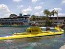 Disneyland’s vibrant yellow submarine glides through sparkling lagoon waters, framed by tropical palms and the park’s iconic attractions.
