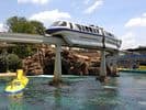 Disneyland's monorail glides over Tomorrowland Lagoon, passing the classic yellow Submarine Voyage and scenic rocky backdrop.