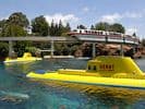 Submarine Voyage’s bright yellow submarines glide through sparkling blue water as the Disneyland Monorail crosses above.