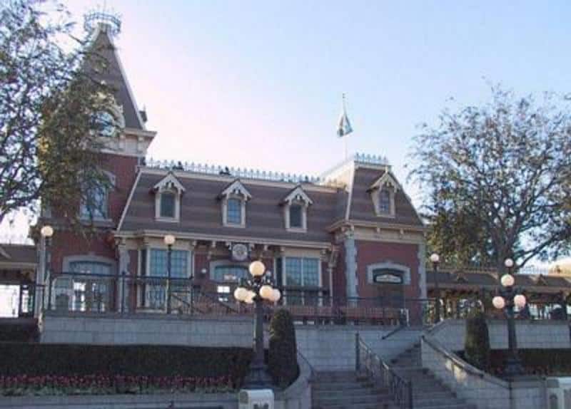 The iconic Victorian train station welcomes guests to Main Street, U.S.A., with charming stairs, lamp posts, and trees—picture perfect!.