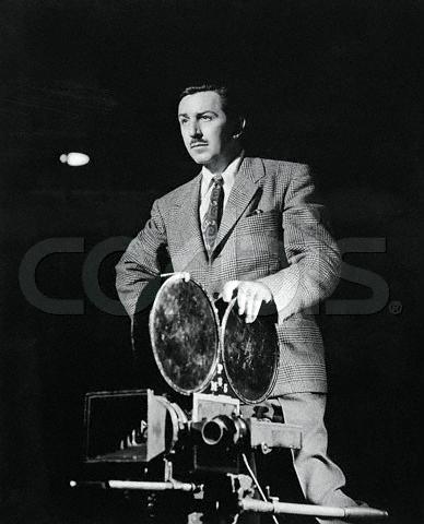 A suited filmmaker behind a vintage camera, holding reels—capturing Disney magic or recording the opening of Disneyland.