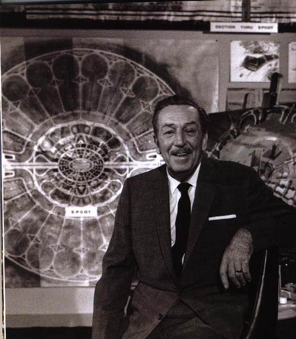 Walt Disney, in a suit, smiles at the camera before his iconic EPCOT blueprint, capturing his visionary dreams for Disney fans.