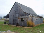 Weathered gray wooden barn with a sloped roof on green grass, echoing the nostalgic Disney hometown charm from the museum.