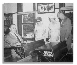 Three Universal Studios team members pose, smiling, beside a host at a vintage school desk inside a themed classroom attraction.