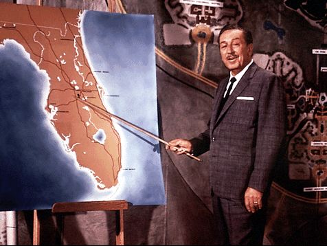 Walt Disney in a suit points to a map of Florida, revealing his vision for the future site of Walt Disney World Resort.