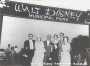 Disney fans gather beneath the "Walt Disney Municipal Park" sign, honoring Walt in his childhood town near the Hometown Museum.