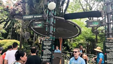 Guests line up for a theme park ride beneath digital displays showing the current standby entrance and estimated wait times.