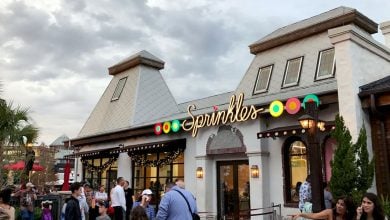 Guests line up outside Sprinkles bakery, drawn by its vibrant marquee and twinkling lights, ready for sweet treats and fun.
