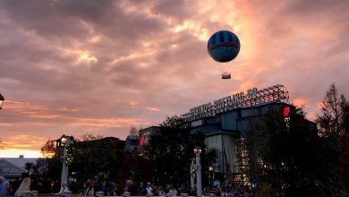 A hot air balloon drifts above CityWalk at sunset, casting color over bustling shops beneath vibrant evening clouds.