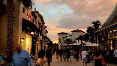 Bustling promenade at sunset with visitors strolling past palm trees, lively shops, and vibrant entertainment venues.