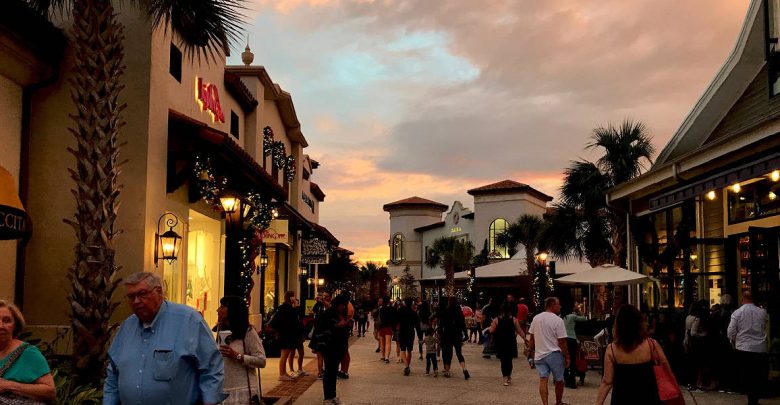 Bustling promenade at sunset with visitors strolling past palm trees, lively shops, and vibrant entertainment venues.