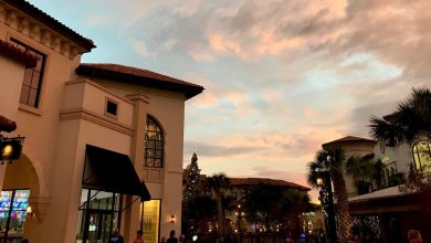 Guests wander along festively adorned Main Street at sunset, surrounded by twinkling lights and a vibrant sky.