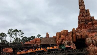 Big Thunder Mountain Railroad train races through dramatic red rocks and wild west scenery beneath a moody, cloud-filled sky.