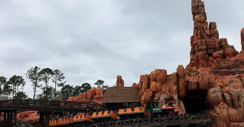 Big Thunder Mountain Railroad train races through dramatic red rocks and wild west scenery beneath a moody, cloud-filled sky.